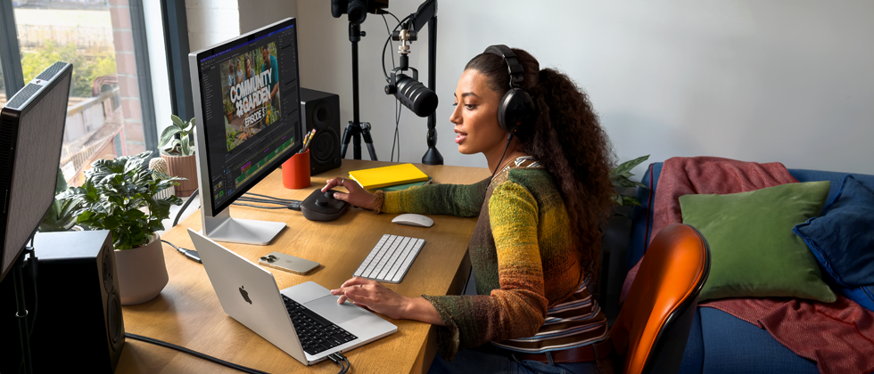 Žena u svom domu radi za stolom s MacBookom Pro povezanim na dva vanjska zaslona, nosi slušalice i govori u mikrofon