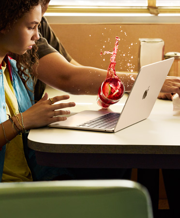 En person rækker ud efter noget på en restaurant og spilder sin drik ud over en åben MacBook