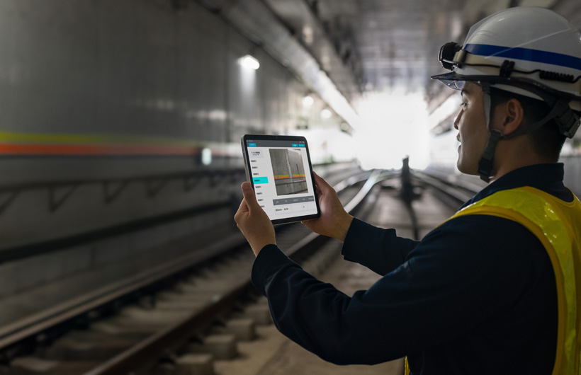 Um funcionário de manutenção nos túneis do metrô de Tóquio usa um iPad para capturar uma imagem dos trilhos enquanto um colega observa.